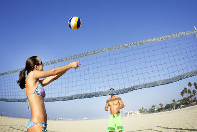 Couple playing beach volleyball against clear sky