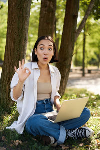 Portrait of young woman using laptop while sitting in forest