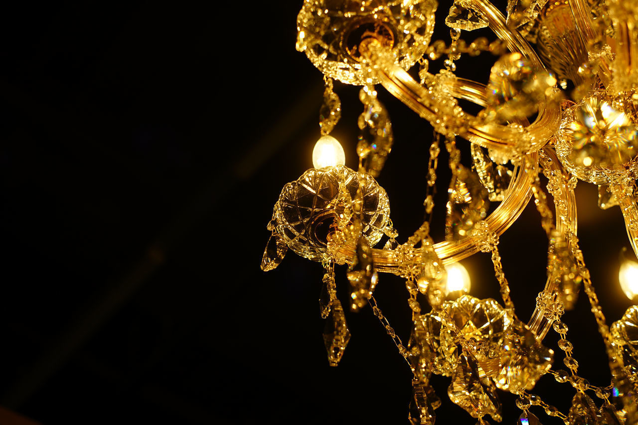 LOW ANGLE VIEW OF ILLUMINATED CHANDELIER HANGING AGAINST BLACK BACKGROUND