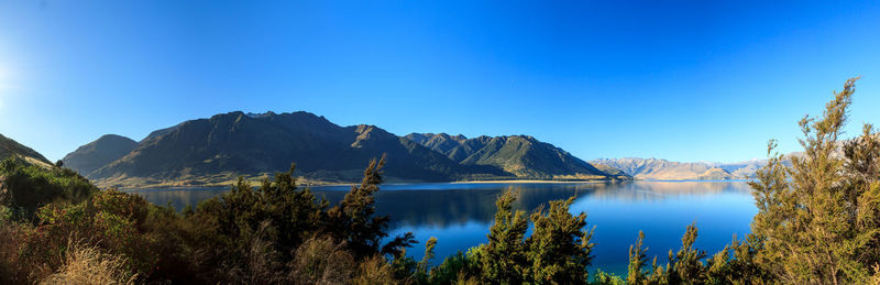 Scenic view of lake and mountains against clear blue sky