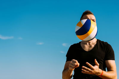 Low angle view of man standing against blue sky with a volleyball in mand