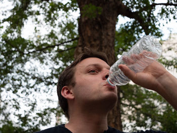 Low angle portrait of man drinking glass against trees