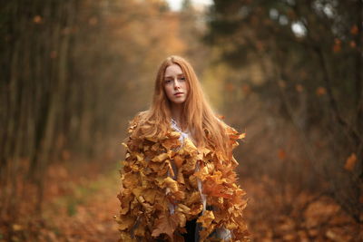 Portrait of young woman standing by tree in forest