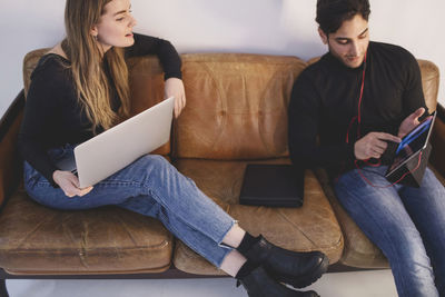 High angle view of male and female bloggers using digital tablet while sitting on sofa at office