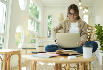 Young woman using laptop chatting online sitting in home living room.