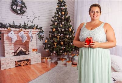 Portrait of smiling woman standing by christmas tree