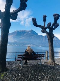 Rear view of bench in park by sea against sky