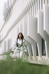 Astronaut wearing space suit holding helmet walking by building