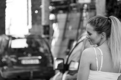 Rear view of young woman with long blond hair while standing by cars