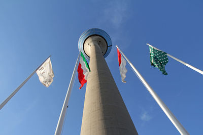 Low angle view of rheinturm with flags against sky