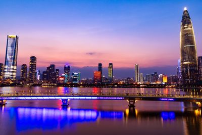 Illuminated buildings by river against sky in city