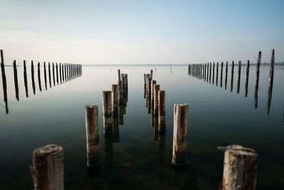 Wooden posts on pier in lake against sky