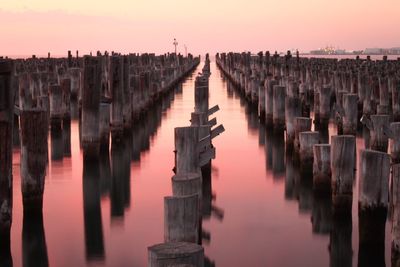 Wooden posts in sea at princes pier during sunset