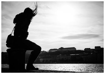 Woman sitting bollard at pier against sky