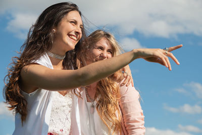 Side view of young woman with arms raised against sky