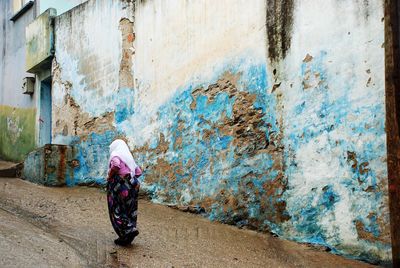 Rear view of woman walking on street against weathered wall