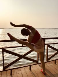 Woman dancing by railing and sea against sky