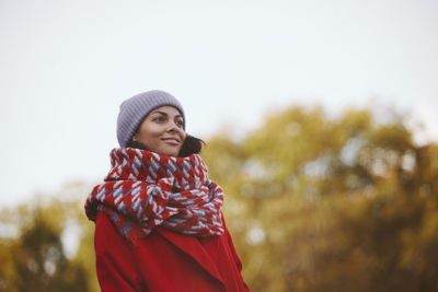 Portrait of young woman wearing hat standing against trees