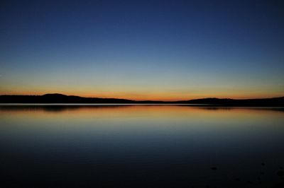 Lake with silhouetted mountains against cloudy sky