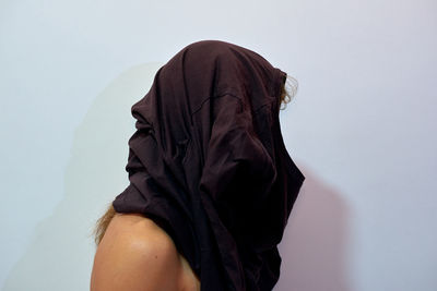 Side view of man with covered face standing by wall at home