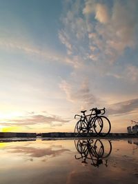 Bicycle by lake against sky during sunset