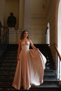 Smiling beautiful young woman wearing dress while standing on staircase