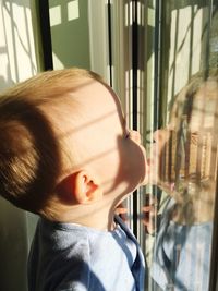 Close-up of cute baby boy touching reflection on glass window