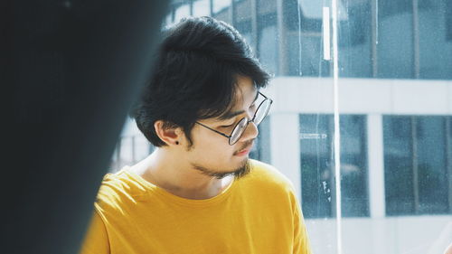 Close-up of young man wearing eyeglasses standing against glass window