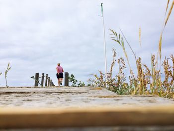 Rear view of woman running on pier against sky