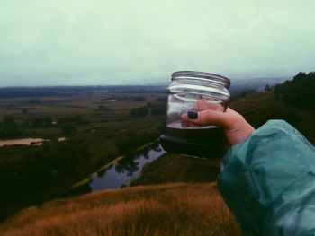 Midsection of woman holding drink jar on field against sky