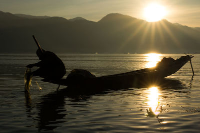 Silhouette man in sea against sky during sunset