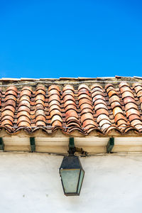 Low angle view of lantern hanging by wall against blue sky