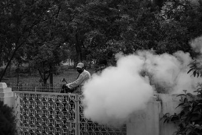 People standing by railing against trees sanitizing the area during covid-19 