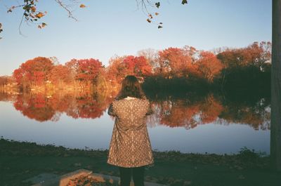 Rear view of woman looking at trees reflection in lake against sky