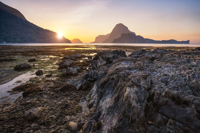 Rock formations at beach against sky during sunset