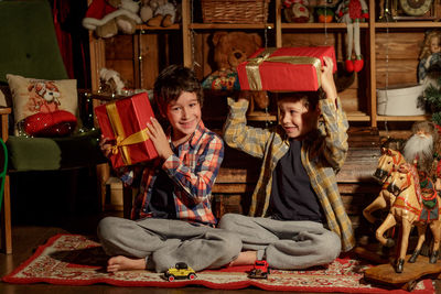 Two real brothers lie in a room with new year's decor near an armchair and look at gifts