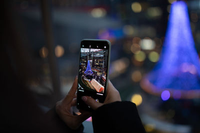 Cropped image of woman photographing decoration on mobile phone at mall