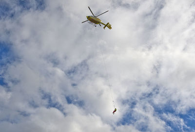 Low angle view of person hanging on rope in flying helicopter