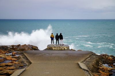 Rear view of men standing on cliff by sea