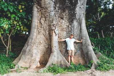 Man standing by tree trunk in forest