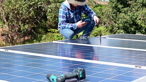 Low section of worker using mobile phone while installing solar panel