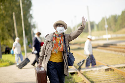 Portrait of positive senior woman wearing a face mask waiting for train due to coronavirus  covid-19