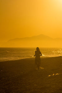 Silhouette man standing on beach against sky during sunset