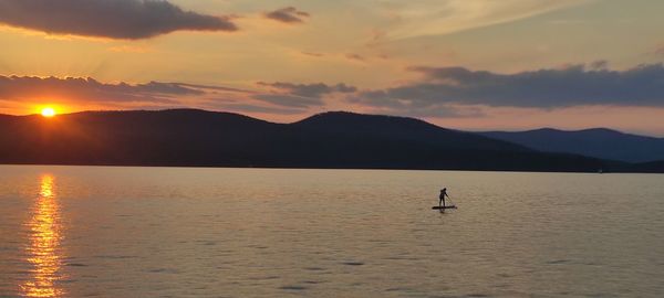 Silhouette person in lake against sky during sunset