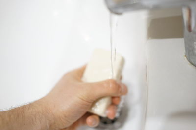 Close-up of hand holding faucet in bathroom