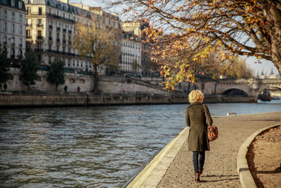 Rear view of young woman walking by seine river