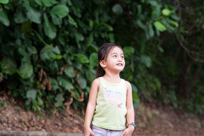 Girl looking away while standing against plants