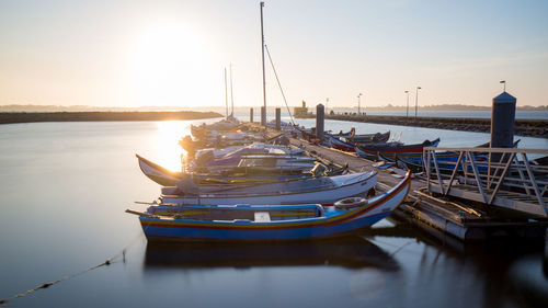 Boats moored at harbor against sky during sunset