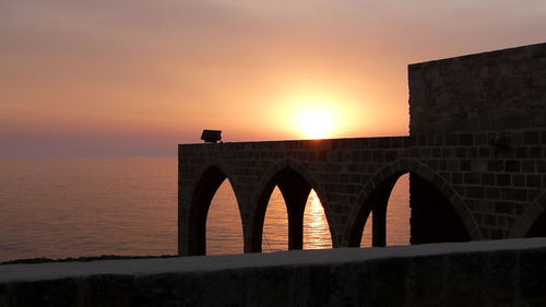 Arch bridge over sea against sky during sunset