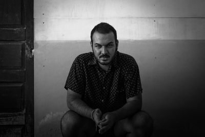 Portrait of young man sitting against wall